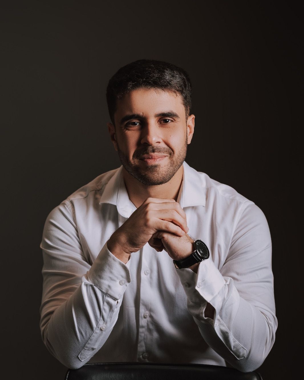Leonardo Ferreira Santos, psicólogo, de camisa branca, apoiado em uma cadeira, com um sorriso calmo
